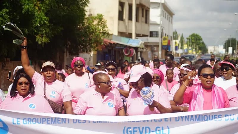 Une foule de femmes en polos et casquettes roses défile derrière la banderole du GFVD-GL, bras levés, lors de la Grande Marche Rose 2025