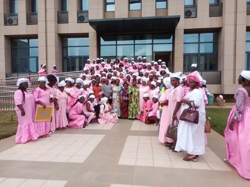 Un grand groupe de femmes vêtues de rose, coiffées de blanc, pose devant un bâtiment officiel
