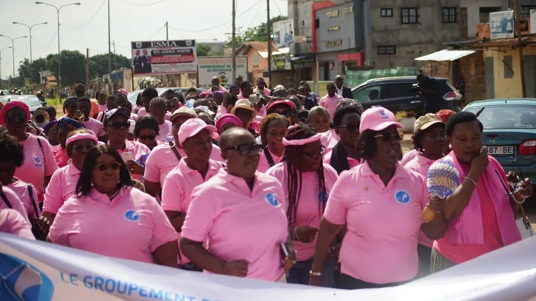Le cortège rose avance derrière la banderole du groupement, le long d’une avenue animée de Lomé